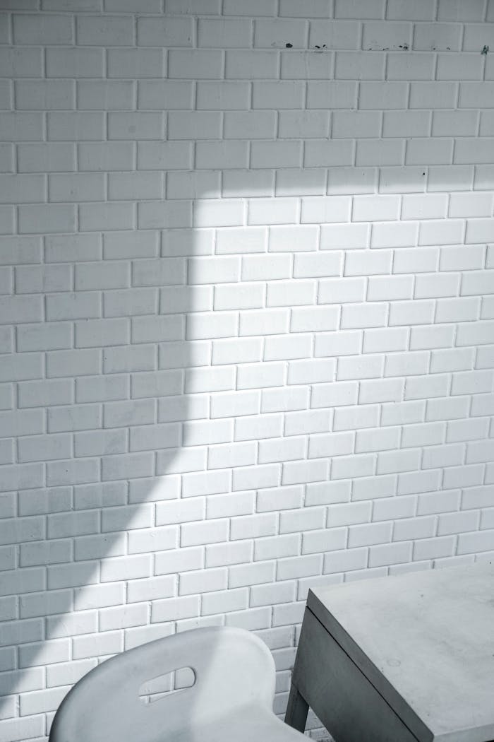 A minimalist white brick wall casting a shadow, paired with a modern chair and table.