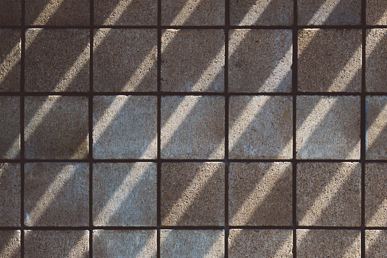 Sunlit shadows create a geometric pattern on textured gray tiles, offering an abstract and minimalistic appeal.